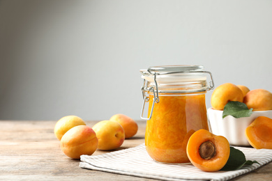 Photo of Jar of apricot jam and fresh fruits on wooden table. Space for text