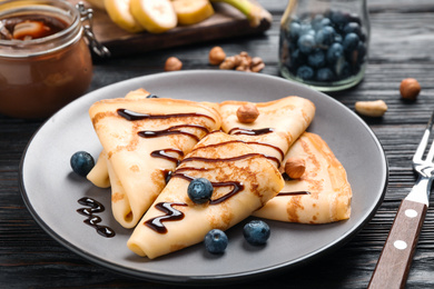 Delicious thin pancakes with chocolate, blueberries and nuts on black wooden table