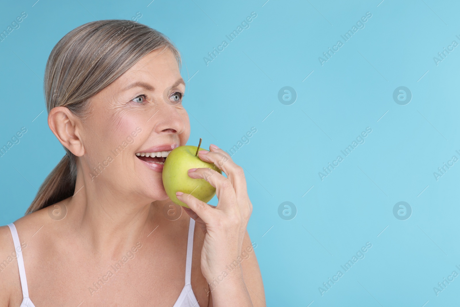 Photo of Beautiful woman eating fresh apple on light blue background, space for text. Vitamin rich food