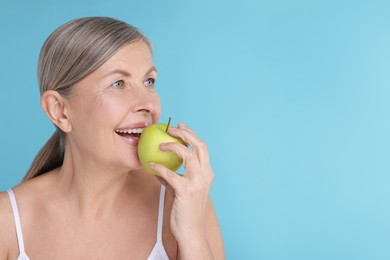 Photo of Beautiful woman eating fresh apple on light blue background, space for text. Vitamin rich food