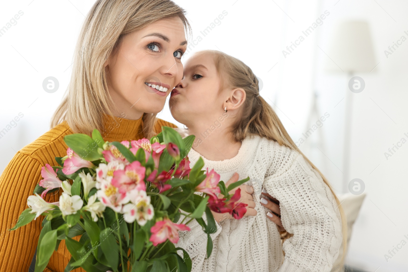 Photo of Little daughter kissing and congratulating her mom with bouquet of alstroemeria flowers at home. Happy Mother's Day