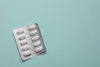 White pills in blister on pale green background, top view. Space for text