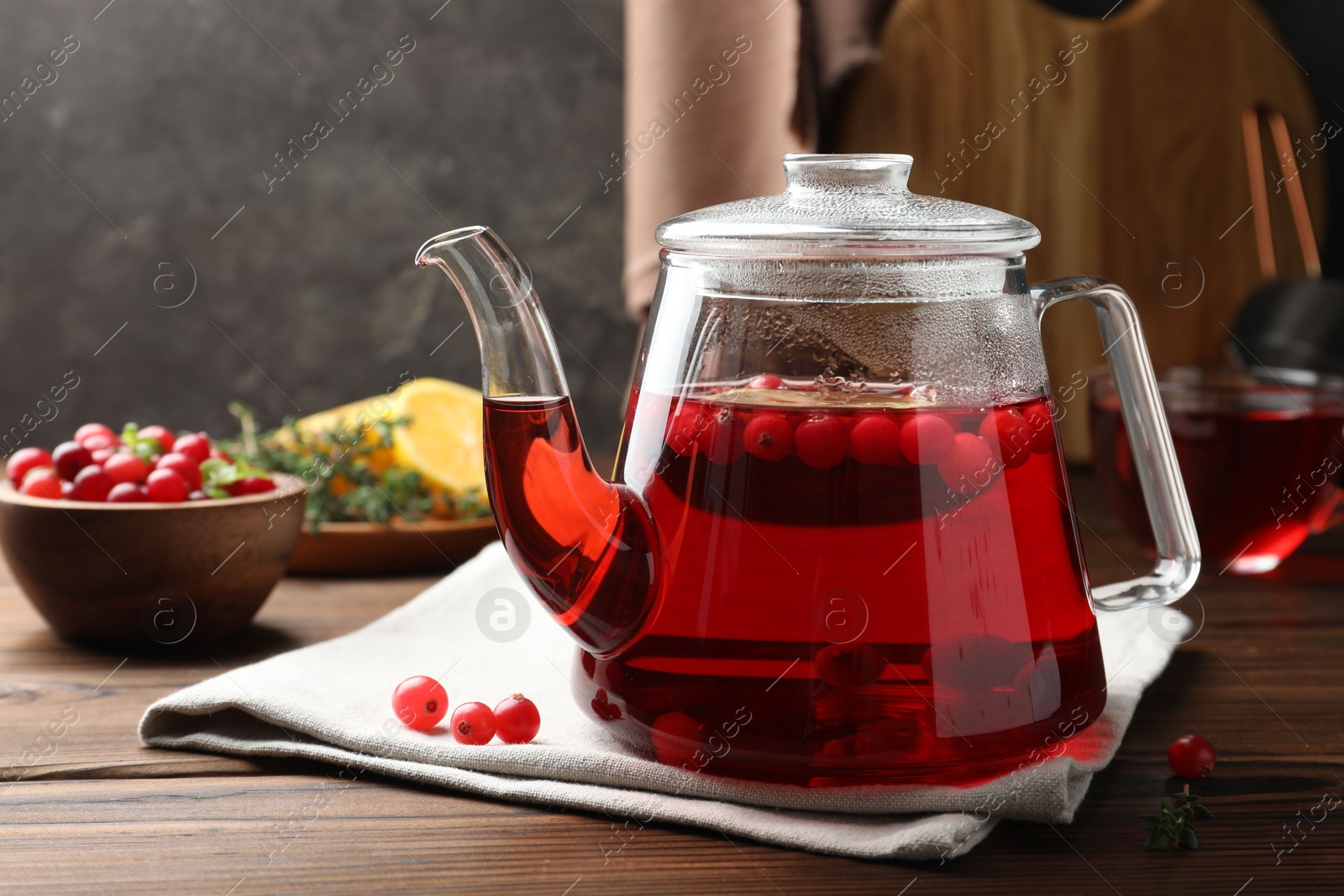 Photo of Tasty hot cranberry tea in teapot and fresh berries on wooden table