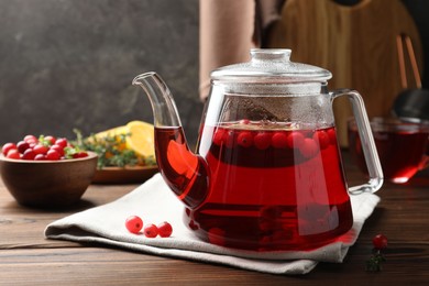 Photo of Tasty hot cranberry tea in teapot and fresh berries on wooden table