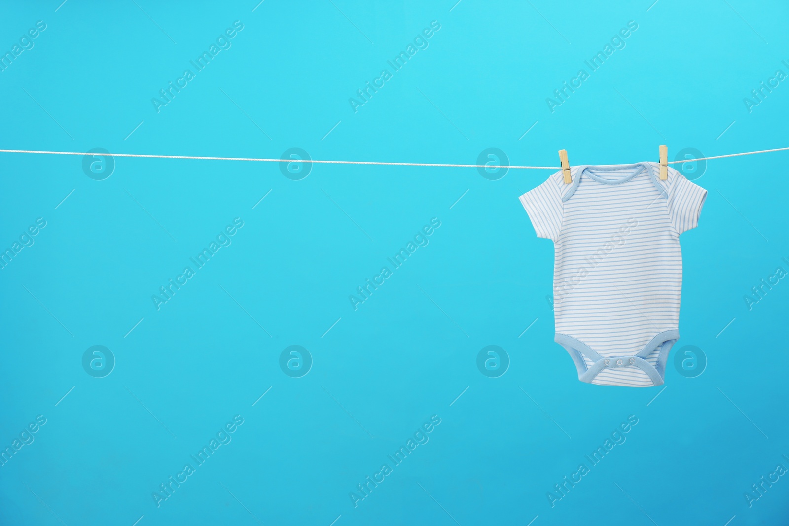 Photo of Baby onesie hanging on clothes line against blue background, space for text. Laundry day