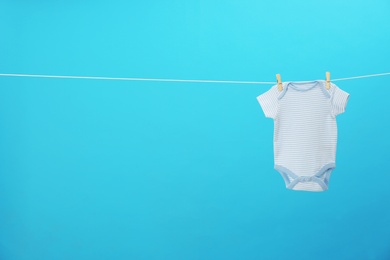 Baby onesie hanging on clothes line against blue background, space for text. Laundry day