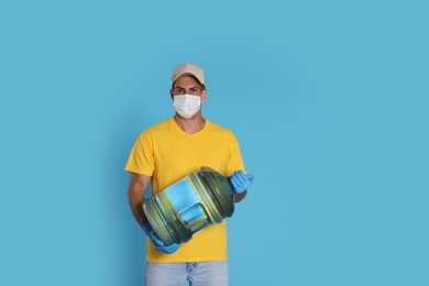 Photo of Courier in medical mask holding bottle for water cooler on light blue background. Delivery during coronavirus quarantine