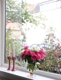 Photo of Vase with beautiful bouquet of roses and candles on windowsill indoors