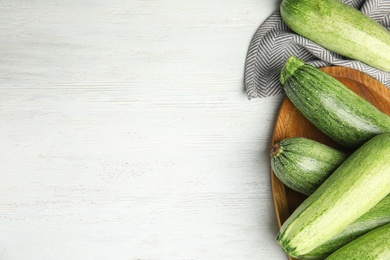 Wooden plate with fresh ripe green zucchinis on white table, flat lay. Space for text