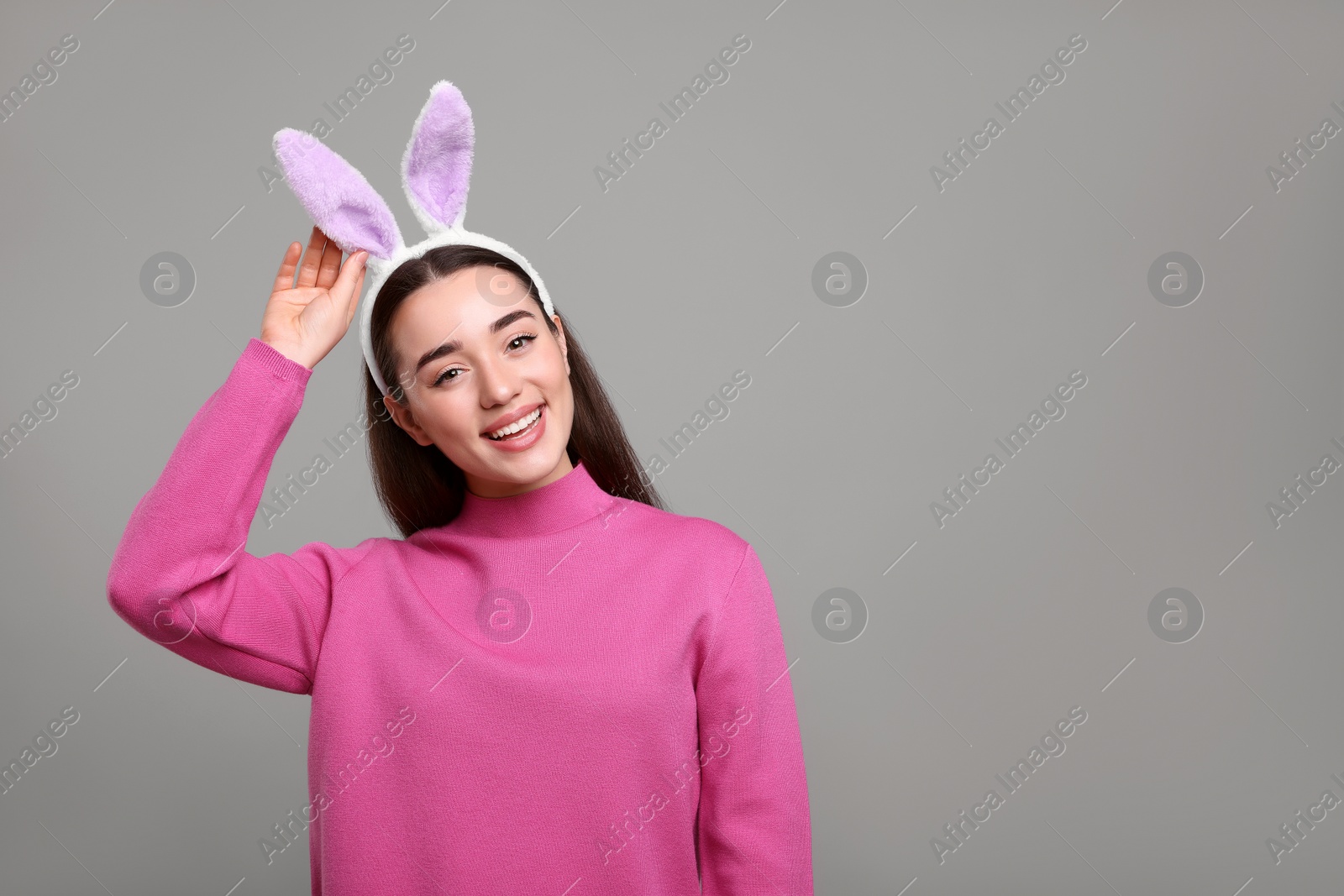 Photo of Happy woman wearing bunny ears headband on grey background, space for text. Easter celebration