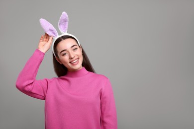 Happy woman wearing bunny ears headband on grey background, space for text. Easter celebration