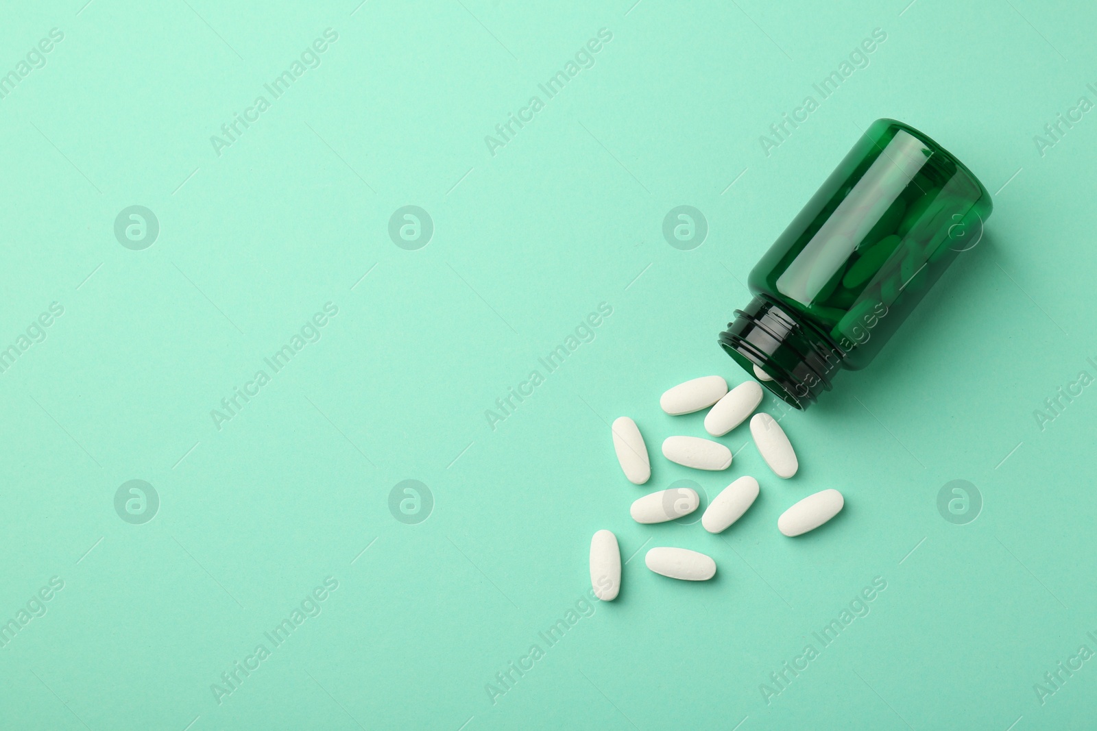 Photo of Vitamin pills and bottle on mint color background, top view. Space for text