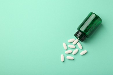 Vitamin pills and bottle on mint color background, top view. Space for text