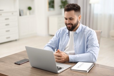 Photo of Young man watching webinar at table in room