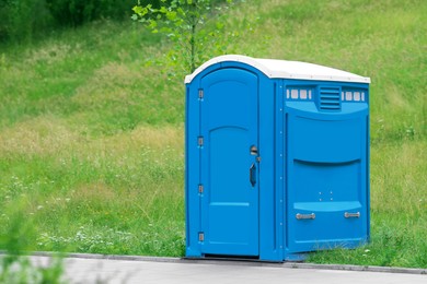 Photo of Blue portable toilet near road in green park