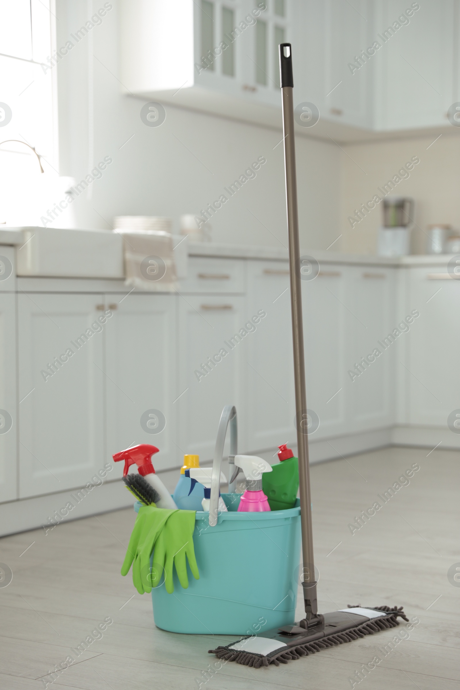 Photo of Mop and plastic bucket with different cleaning supplies in kitchen