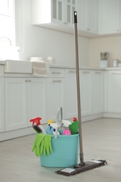 Photo of Mop and plastic bucket with different cleaning supplies in kitchen