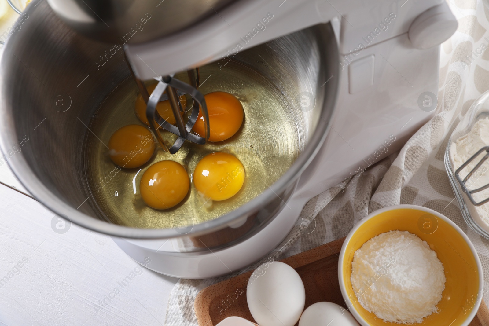 Photo of Making dough. Raw eggs in bowl of stand mixer on white table, closeup