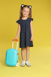 Cute little girl with suitcase on yellow background