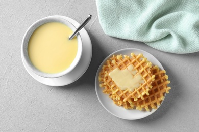 Flat lay composition with bowl of condensed milk and waffles on grey background