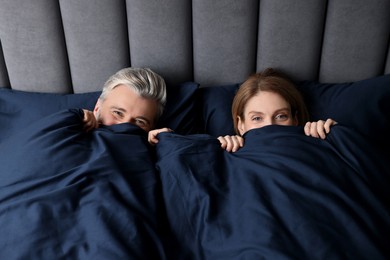Photo of Lovely mature couple hiding together under blanket in bed at home, above view
