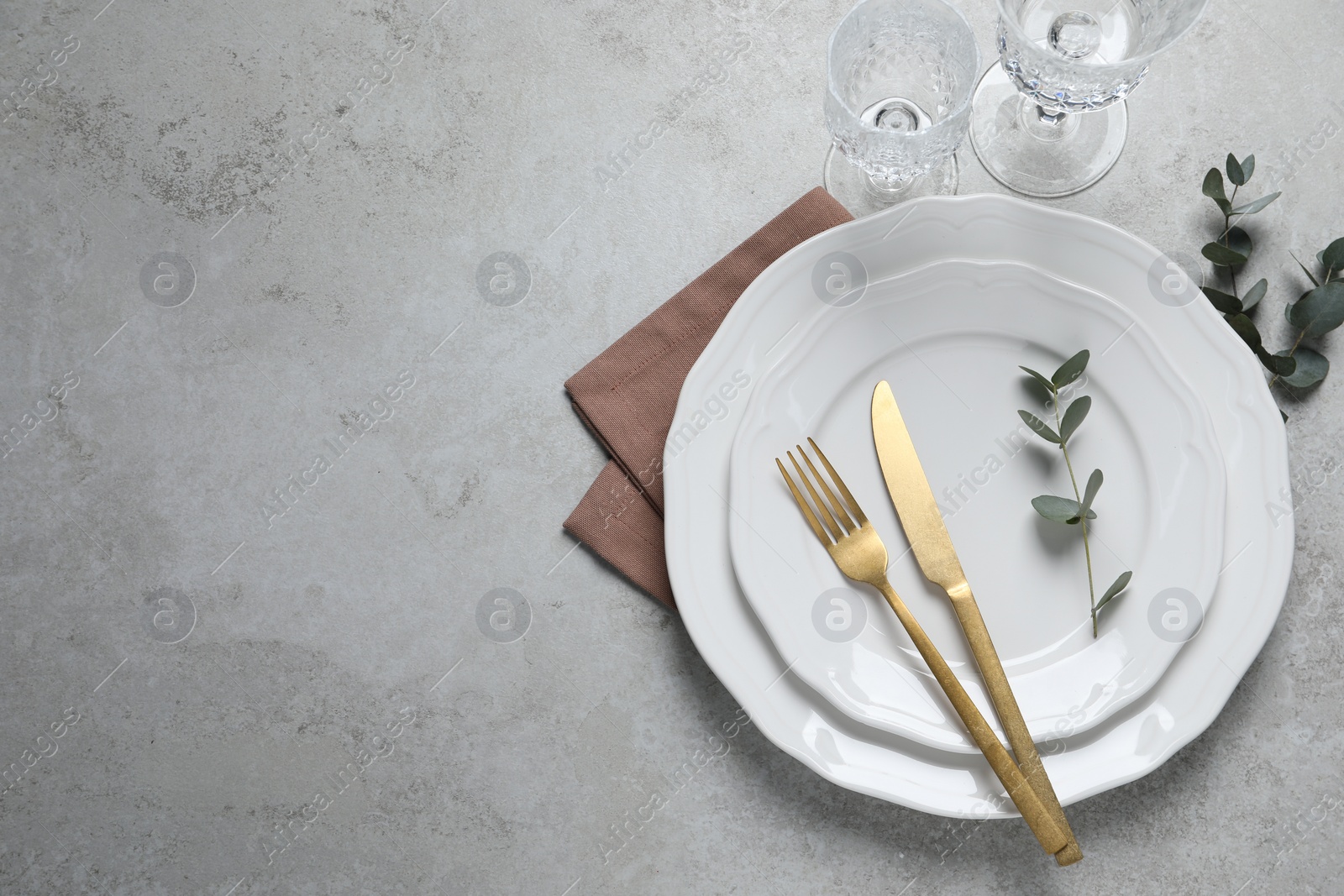 Photo of Stylish setting with cutlery and eucalyptus leaves on light grey table, flat lay. Space for text