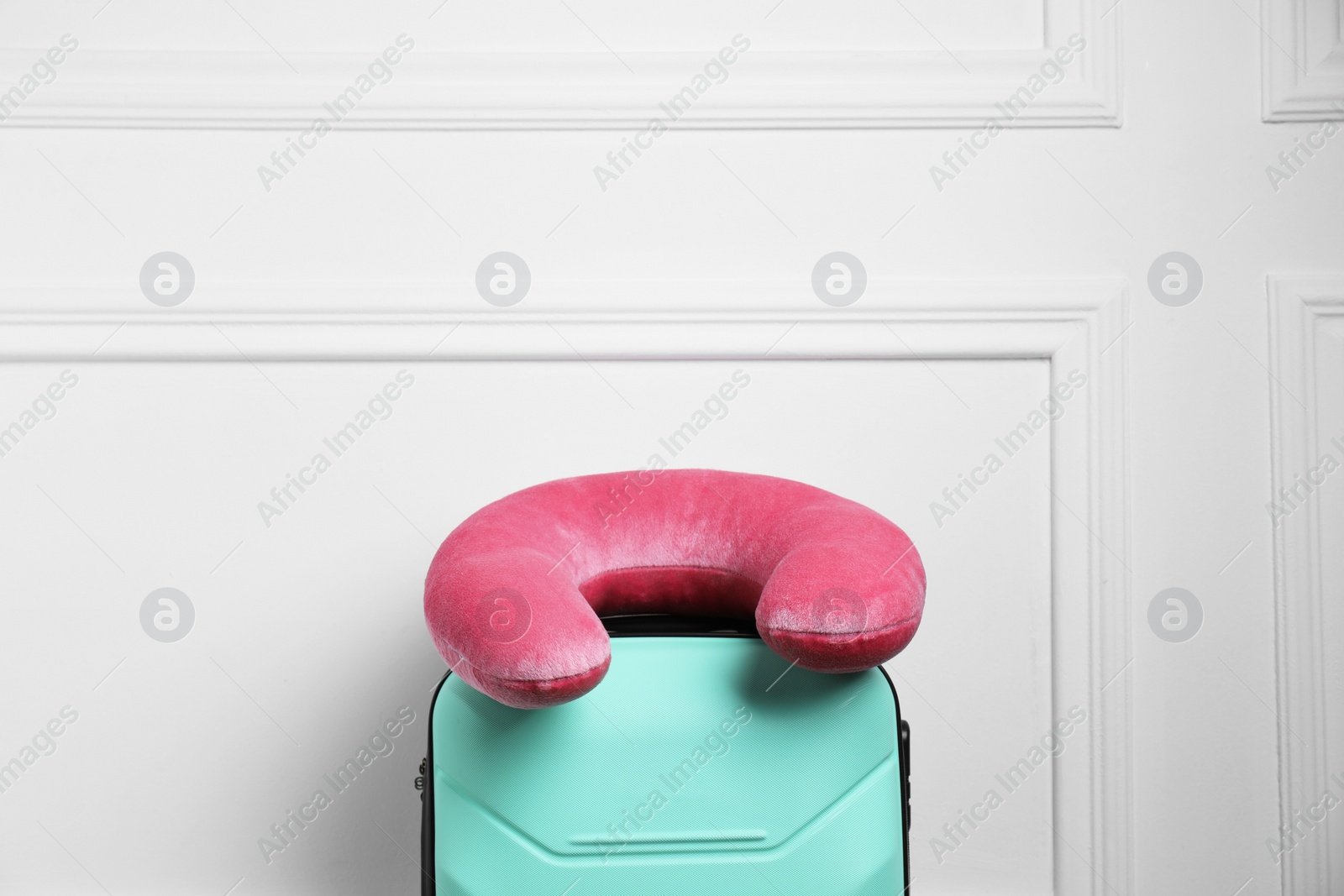 Photo of Pink travel pillow on turquoise suitcase near white wall, space for text