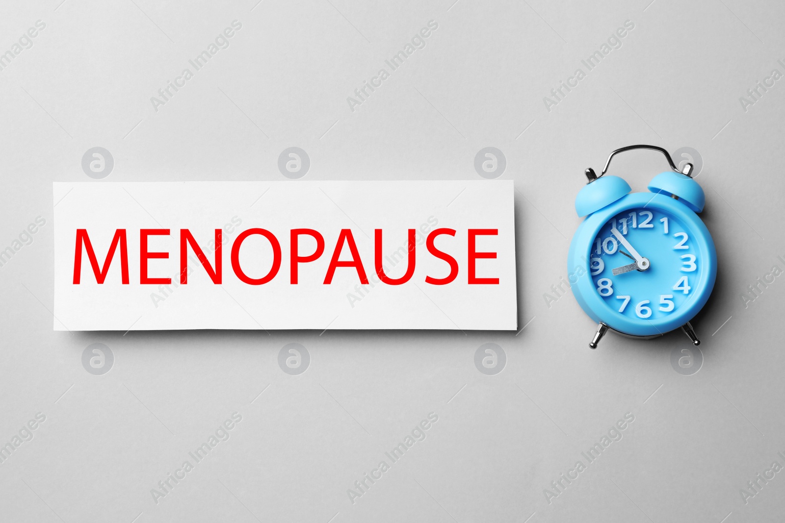 Photo of Card with word Menopause and alarm clock on white background, flat lay