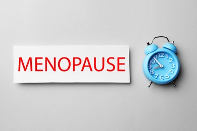 Card with word Menopause and alarm clock on white background, flat lay
