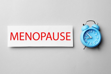 Photo of Card with word Menopause and alarm clock on white background, flat lay