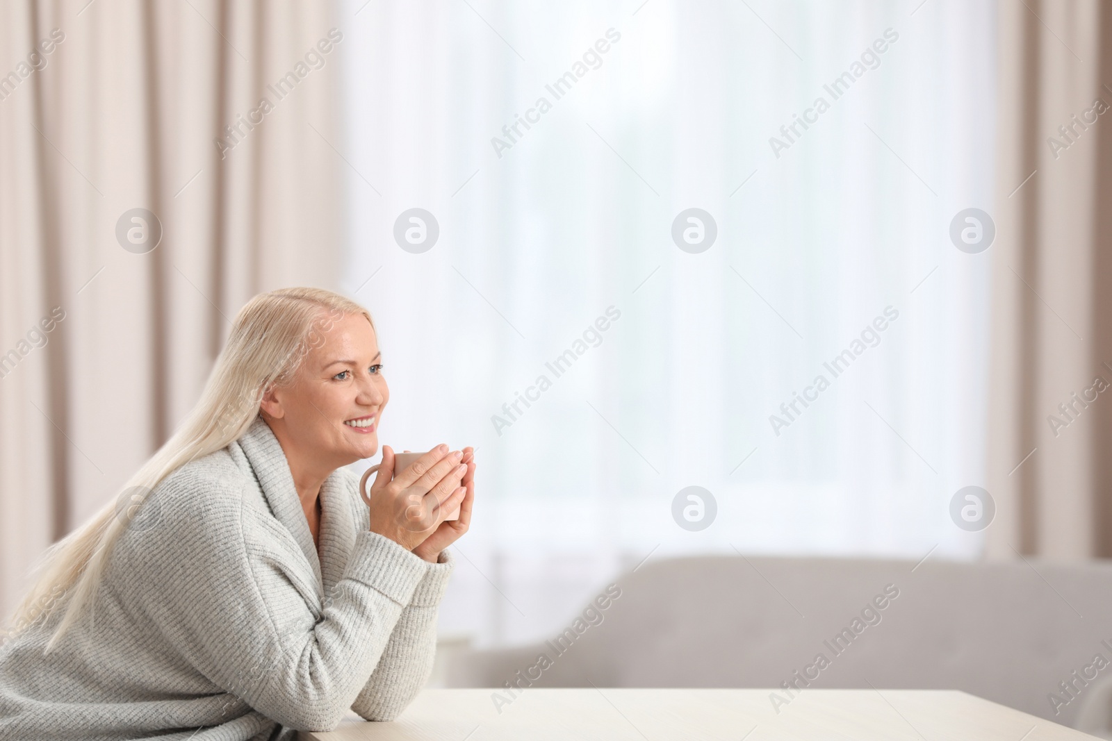 Photo of Portrait of beautiful older woman with cup of tea sitting at table indoors. Space for text
