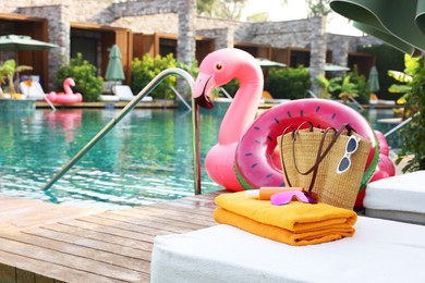 Photo of Beach accessories on sun lounger, inflatable ring and float near outdoor swimming pool, space for text. Luxury resort
