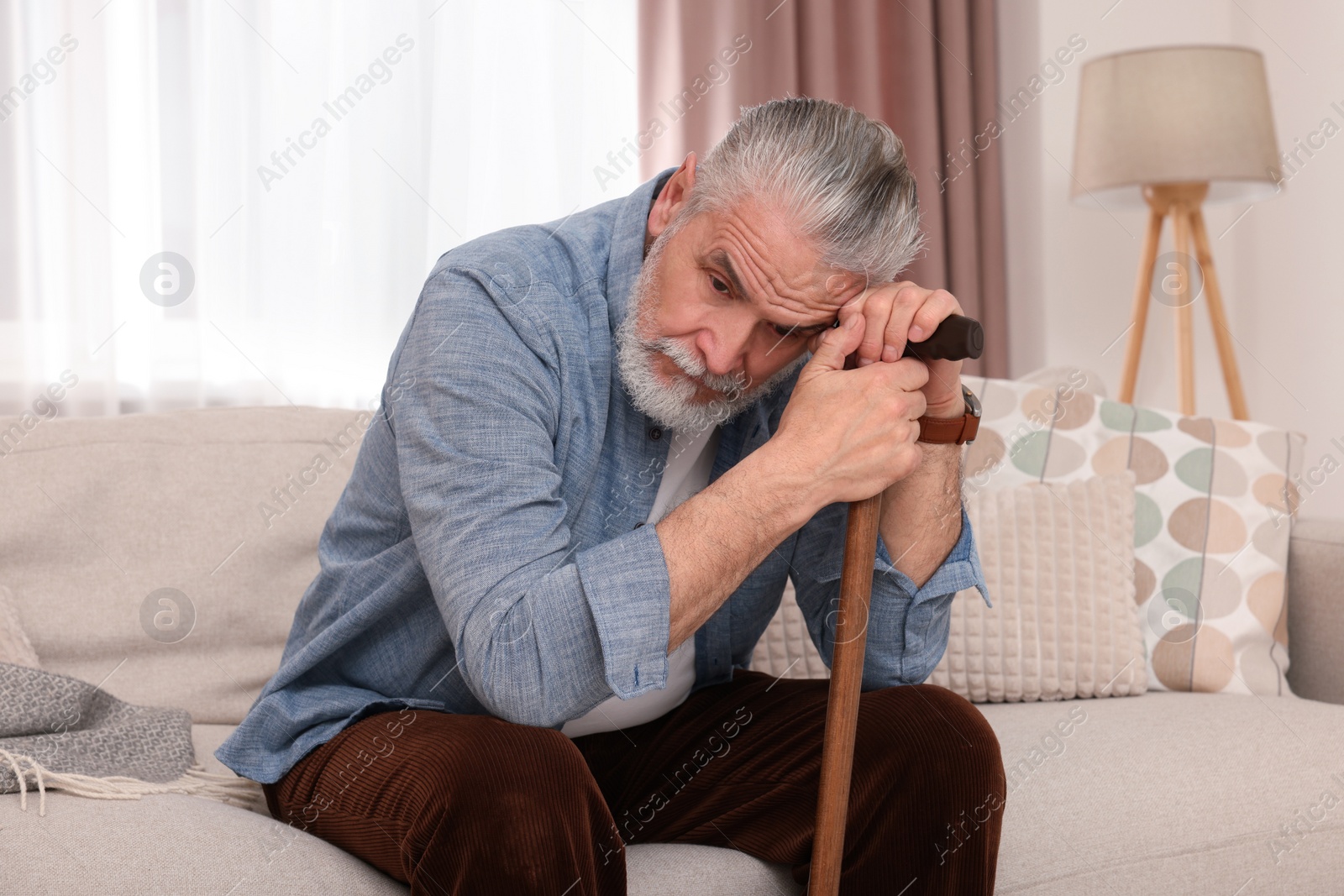 Photo of Senior man with walking cane sitting on sofa at home