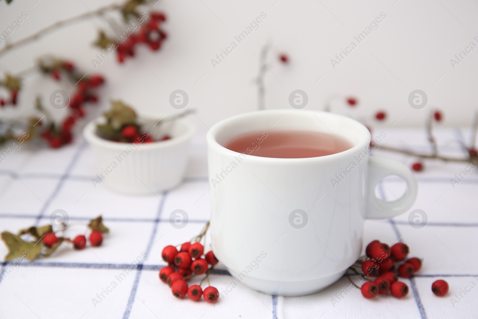 Photo of Cup with hawthorn tea and berries on table, closeup. Space for text