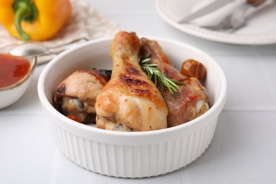 Photo of Delicious roasted chicken drumsticks with rosemary and tomatoes in bowl on white tiled table, closeup
