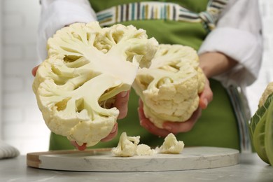 Photo of Woman holding halves of fresh cauliflower at light grey table, closeup