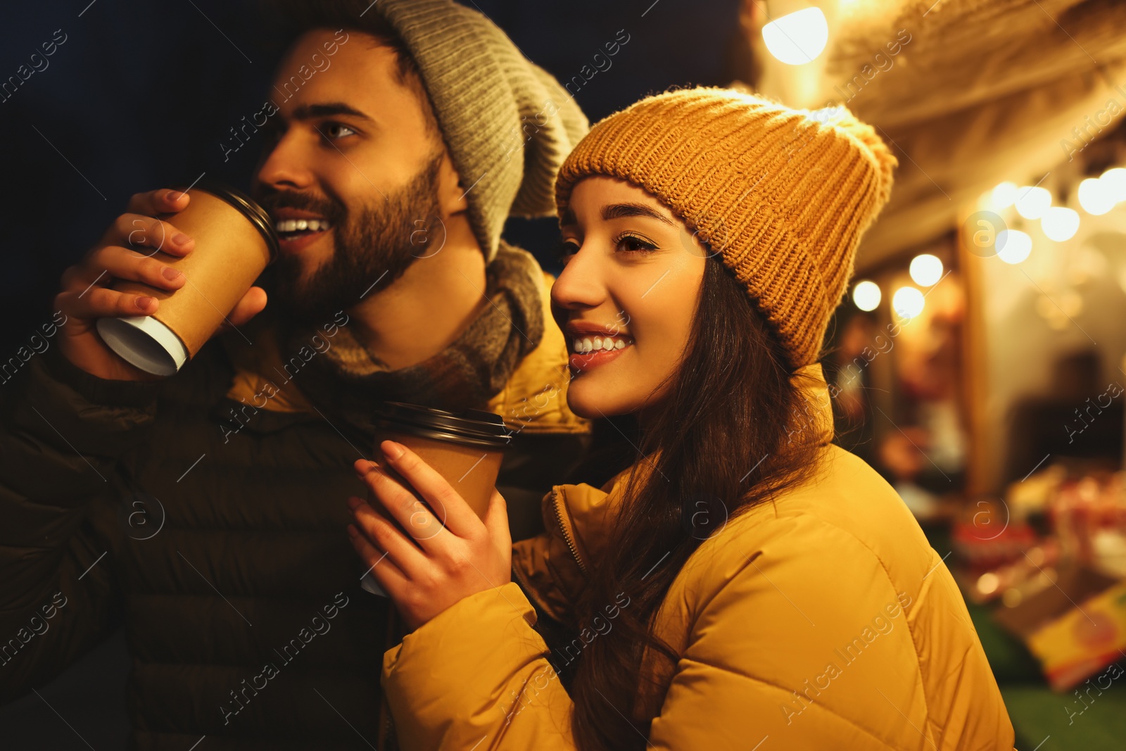 Photo of Lovely couple with cups of hot drinks spending time together at Christmas fair