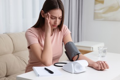 Woman suffering from headache and measuring blood pressure with tonometer at home