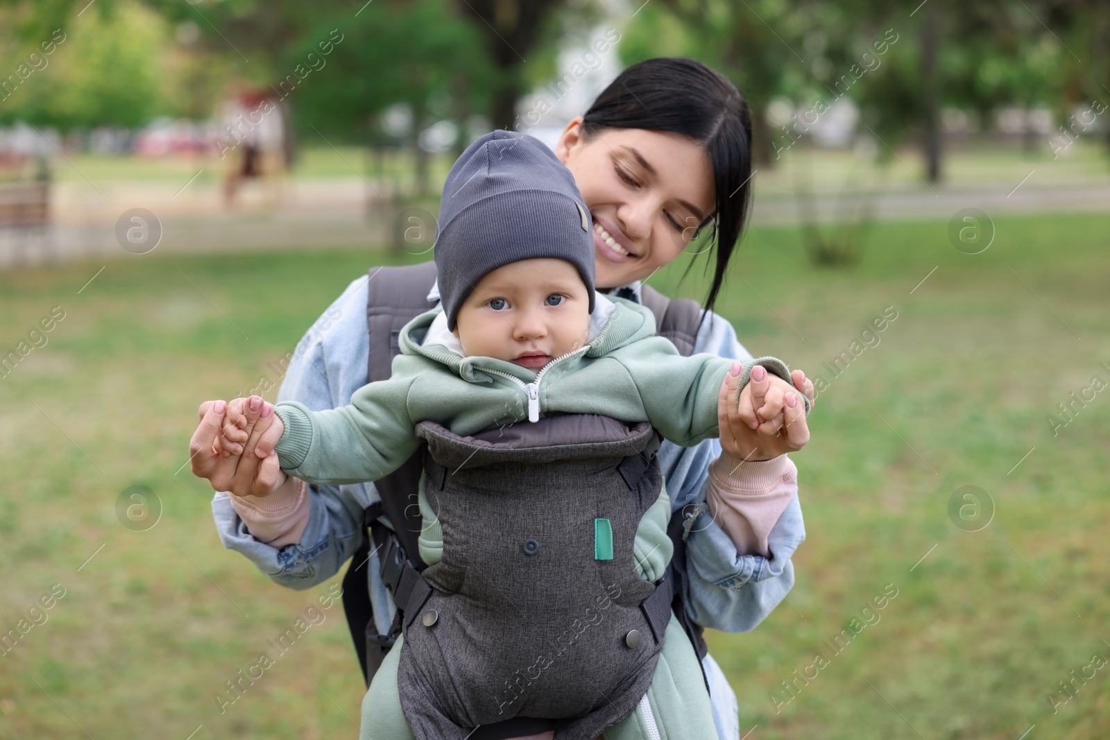 Photo of Mother holding her child in sling (baby carrier) in park