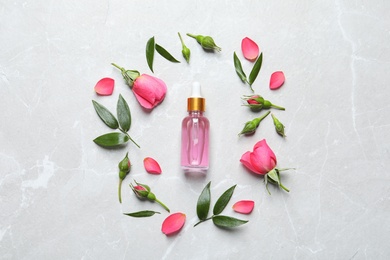 Flat lay composition with fresh flowers and bottle of rose essential oil on table