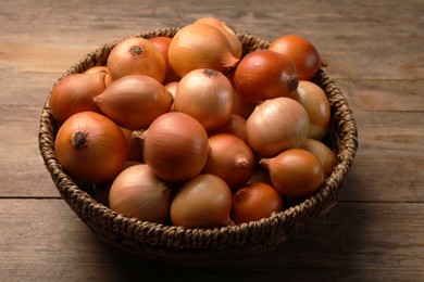 Photo of Wicker basket with many ripe onions on wooden table