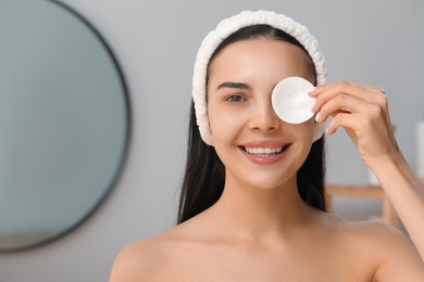 Photo of Young woman using cotton pad with micellar water indoors