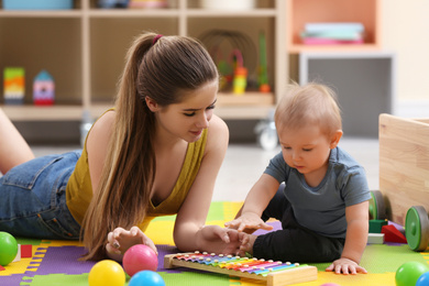 Photo of Teen nanny and cute little baby playing with xylophone at home