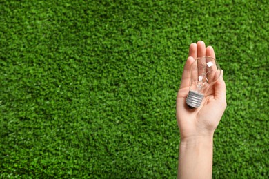 Photo of Woman holding incandescent light bulb over green grass, top view. Space for text