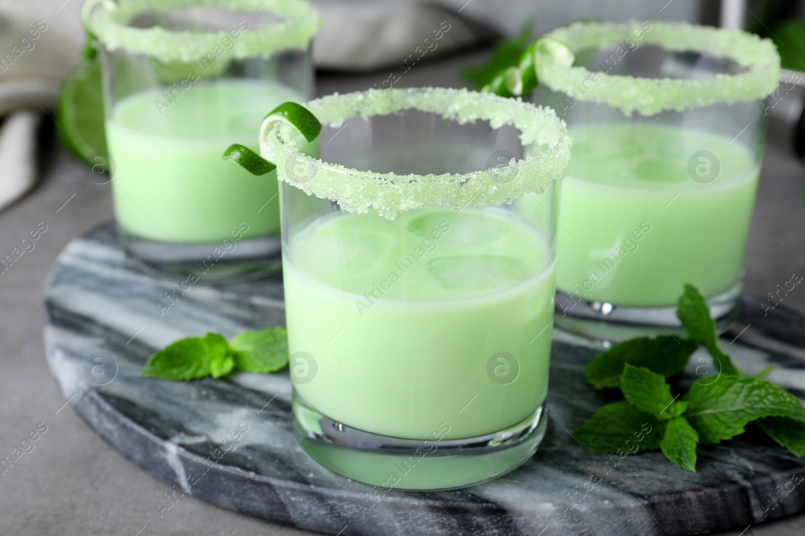 Photo of Delicious mint liqueur with ice cubes and green leaves on grey table, closeup