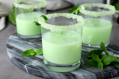 Photo of Delicious mint liqueur with ice cubes and green leaves on grey table, closeup