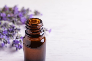 Bottle of essential oil and lavender flowers on white wooden background. Space for text