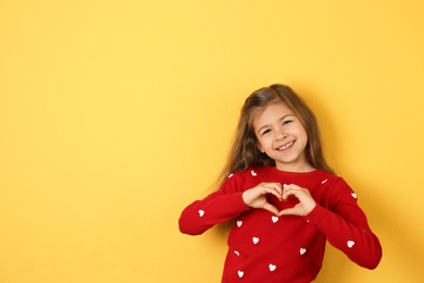 Girl making heart with her hands on color background. Space for text