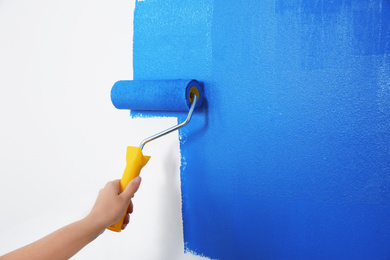 Photo of Woman painting white wall with blue dye, closeup. Interior renovation