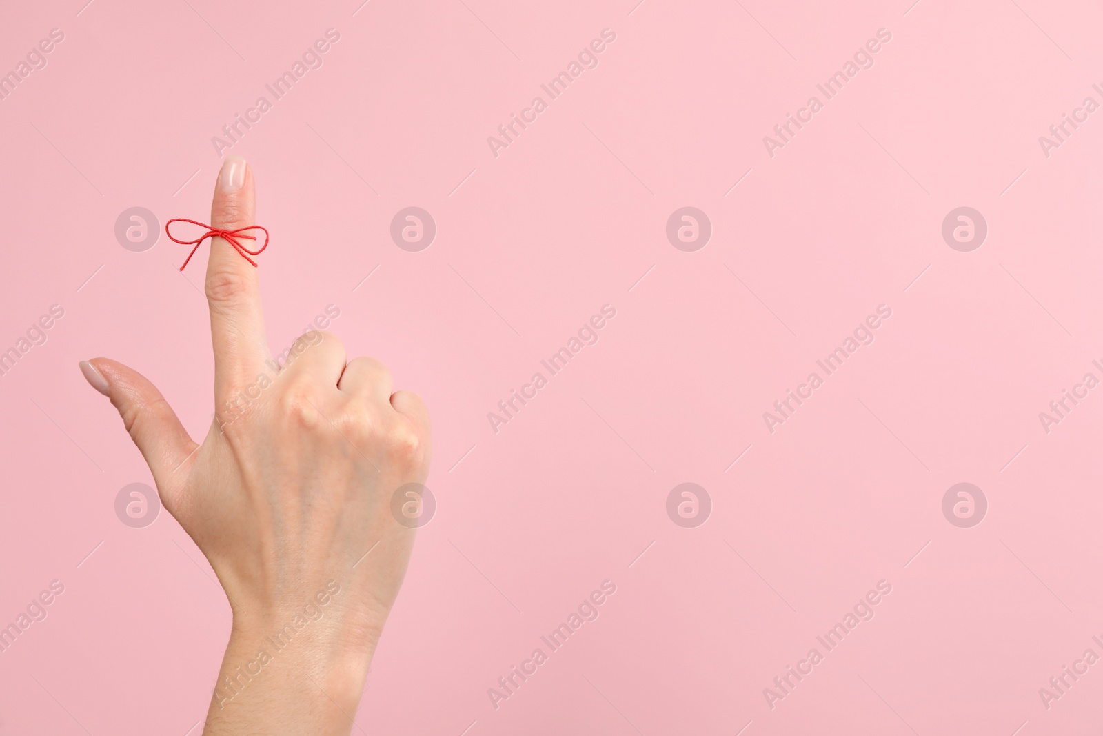 Photo of Woman showing index finger with tied red bow as reminder on pink background, closeup, Space for text